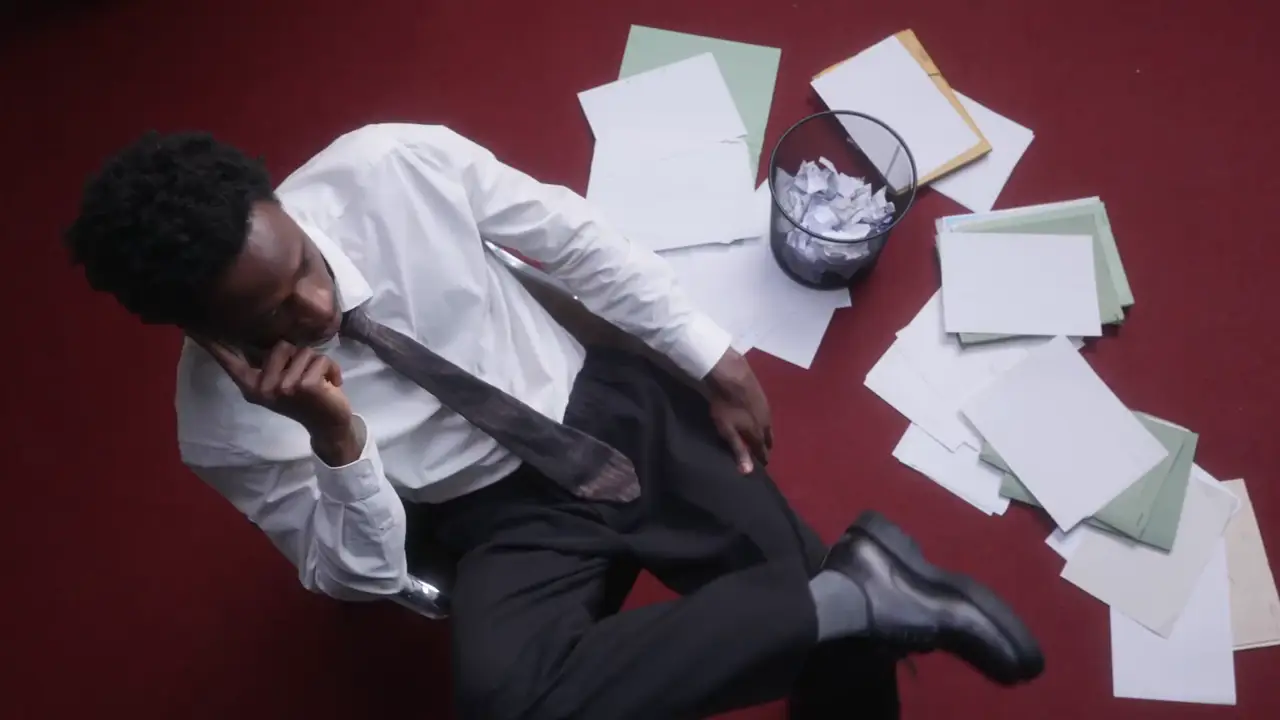 A man sitting on the floor among scattered papers, talking on the phone.